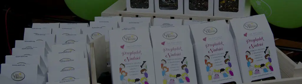 Opakowania herbaty „Przylądek Nadziei” od Czas na Herbatę z ilustracją dzieci, ustawione w rzędach na drewnianych koszykach