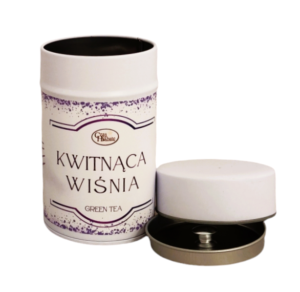 Biała puszka herbaty z napisem "Kwitnąca Wiśnia GREEN TEA", ozdobiona fioletowymi akcentami i z otwartą przykrywką ze srebrnym wnętrzem.