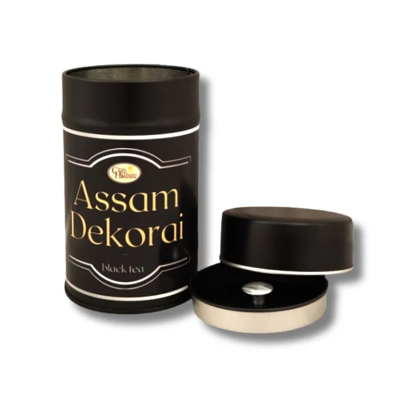 Czarna puszka herbaty Assam Dekorai, obok leżąca pokrywka z metalowym zamknięciem, na białym tle.